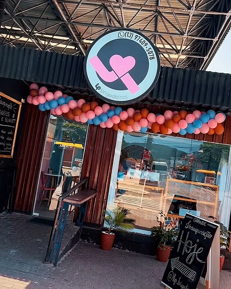 Fachada da L.P Brigadeiros no dia da inauguração, com a placa redonda do logo e o arco de balões rosa e azul